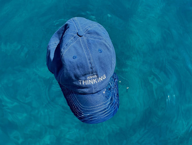 Custom Embroidery with white thread text "don't over think it" on a cool blue dad cap in a swimming pool