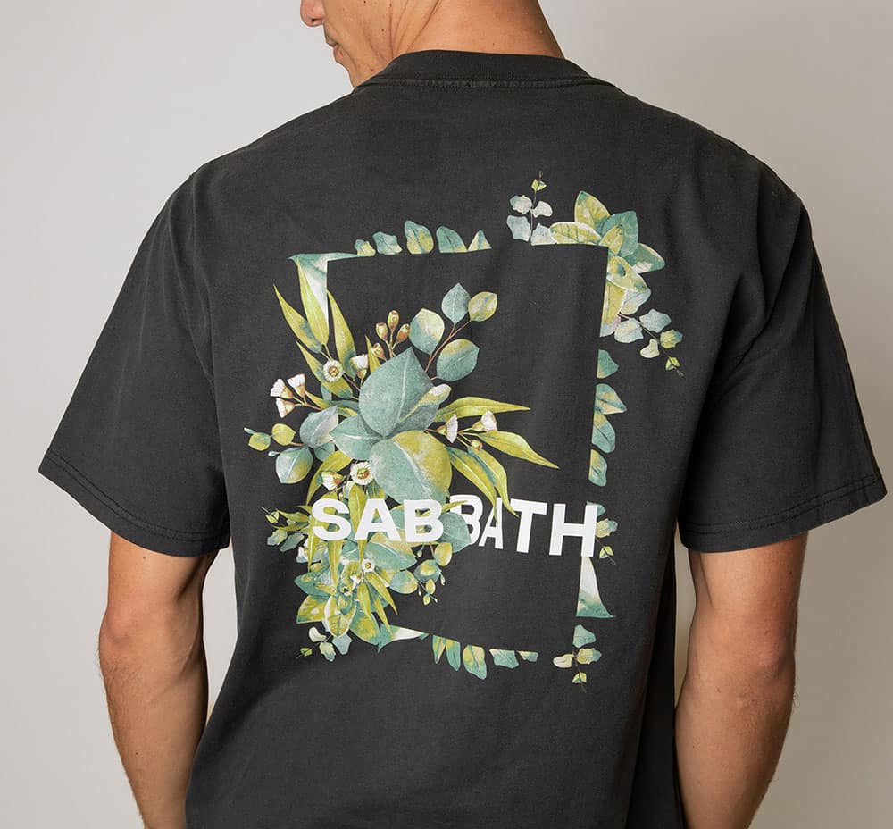 Black T-shirt with a rectangular botanical design featuring green leaves, white flowers, and the text 'SABBATH