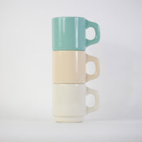 A stack of three customisable ceramic diner mugs in mint green, sand, and cream white against a plain white background.