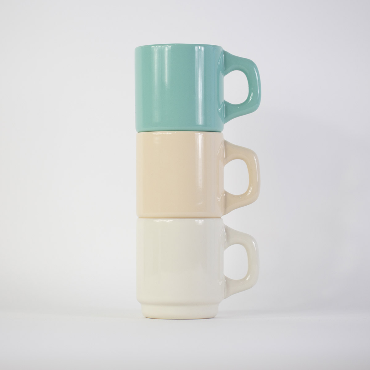 A stack of three customisable ceramic diner mugs in mint green, sand, and cream white against a plain white background.