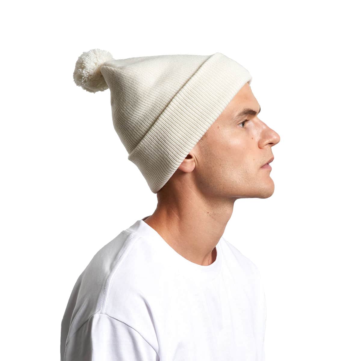 A cozy AS Colour Pom Pom Beanie worn by a male featuring a cuffed hem and a tonal pom pom.