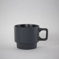 Matte black stackable ceramic coffee mug with a ribbed base and square handle, viewed from the side against a light grey background.